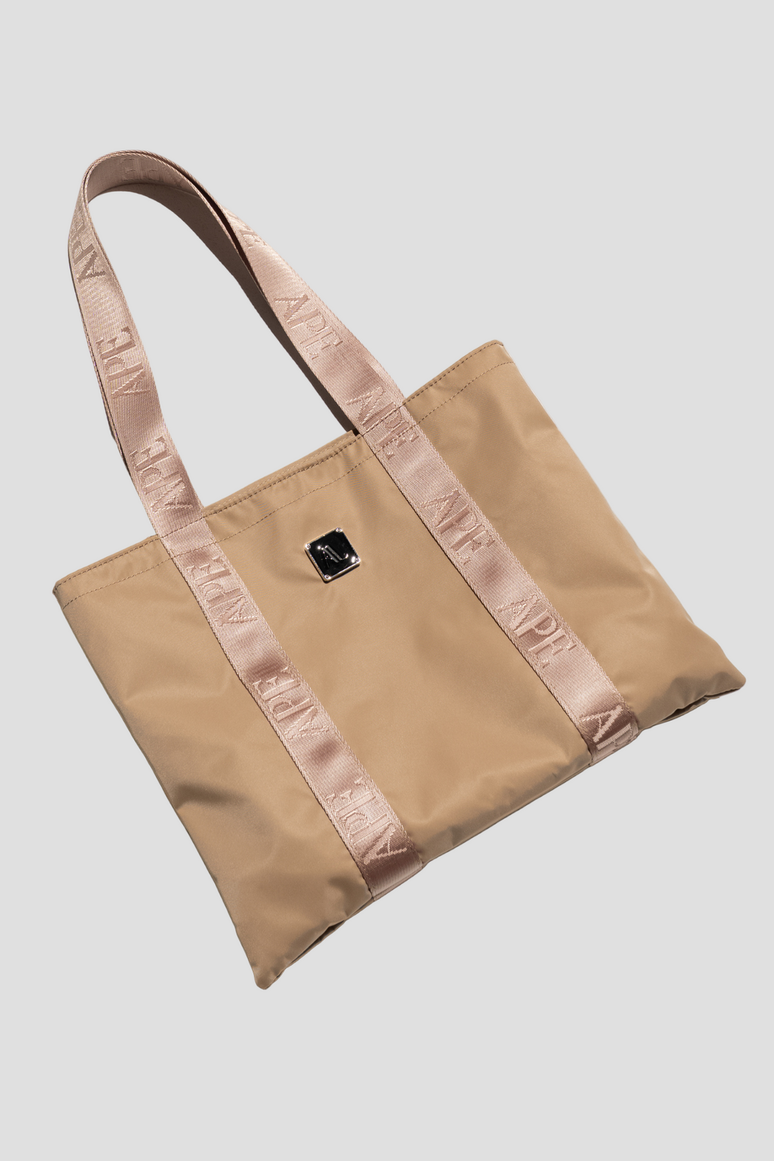 A beige mini tote bag with pink straps and a signature Ape strap detailing, placed against a white background.