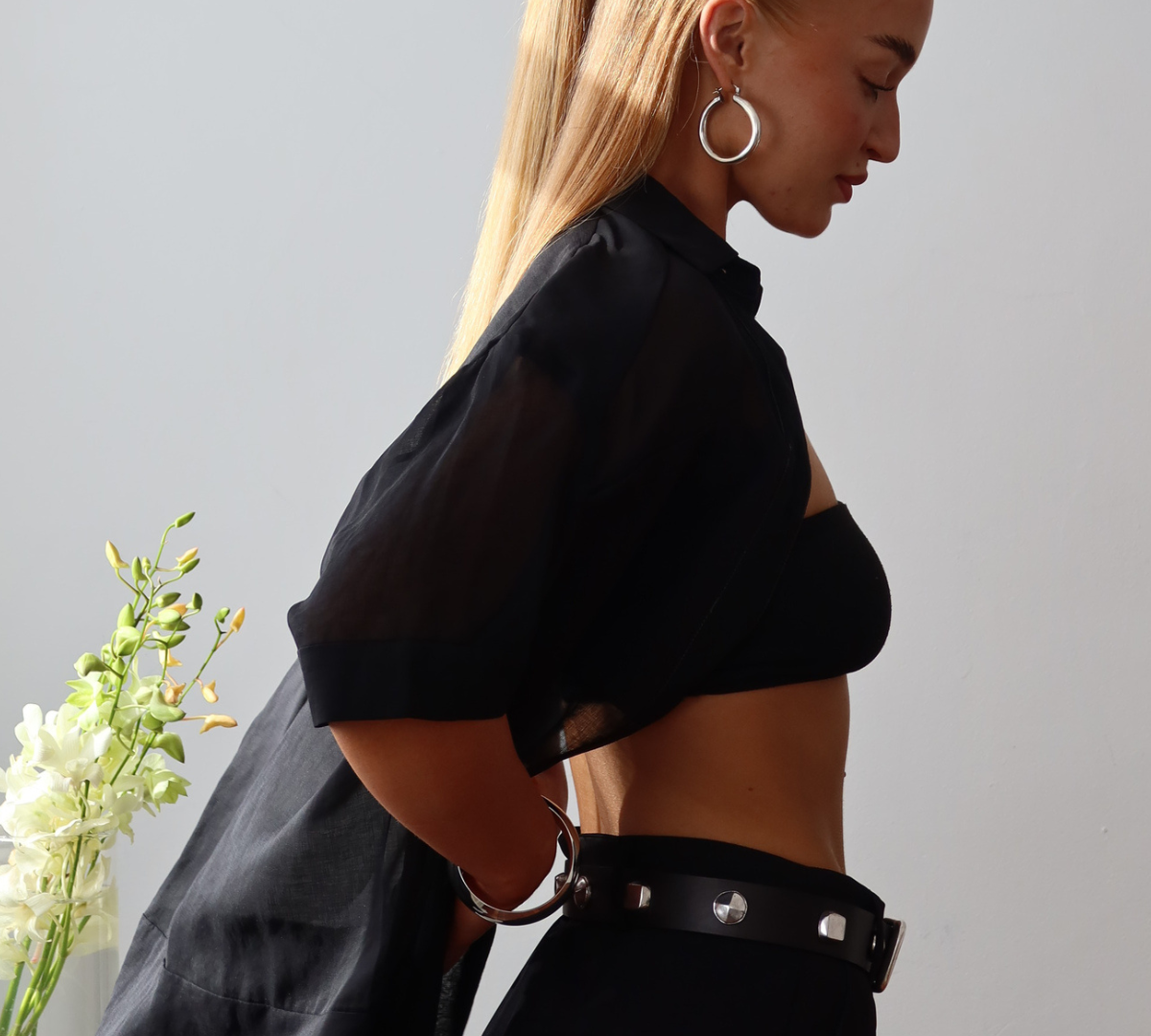 Model in profile wearing a sheer black Ape the Label shirt with a black bandeau and tailored black pants